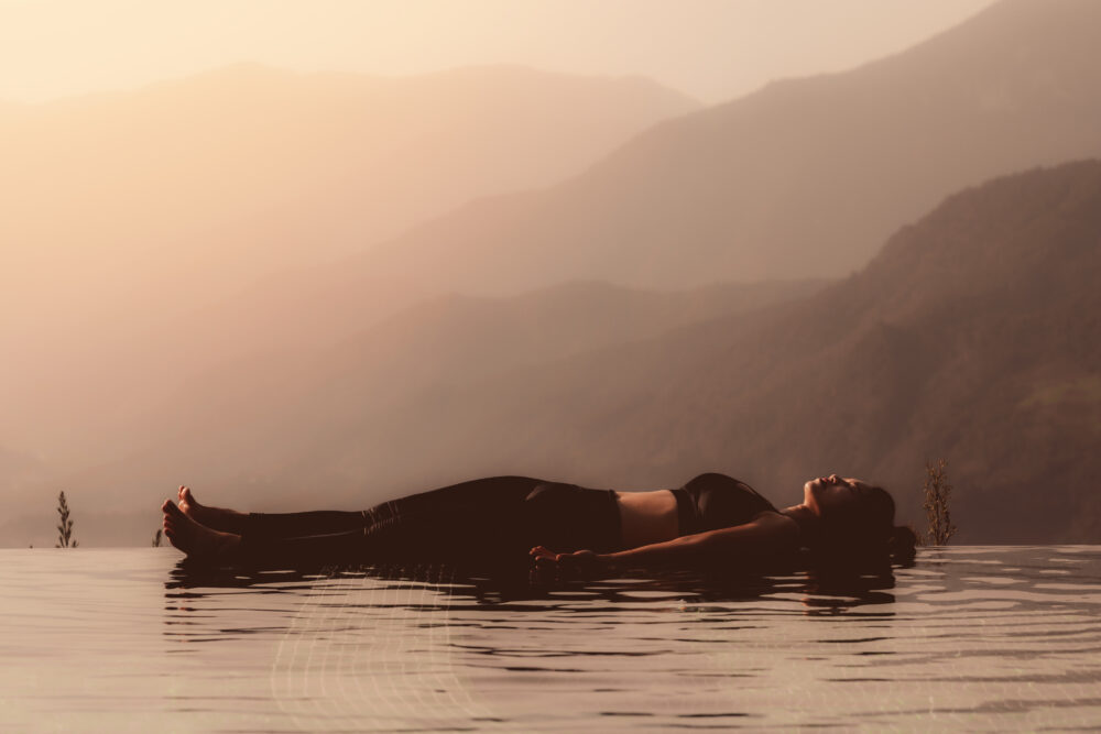 Frau in Shavasana am Pool über Berggipfel vor wunderschönen Naturansichten in Vietnam